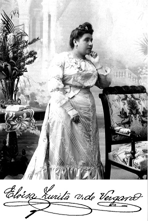 Retrato de Eloísa Zurita de pie, con vestido largo claro, apoyada en un sillón. Abajo, su firma: Eloísa Zurita v. de Vergara.